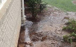Rainwater floods the ground near a building's brick wall during heavy rainfall and energy-efficient sliding doors
