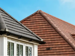 Image of two  roofs. The roof in front is grey on top of a white house, The roof behind has brown roosing tiles 