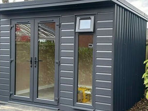 Black garden room in the garden surrounded by bushes