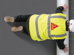 Image of a man with a yellow high vis jacket with Sika logo rolling out waterproofing products.