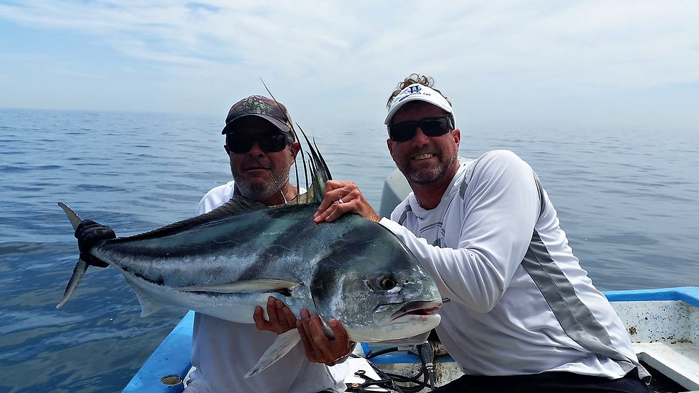 Two anglers on a panga holding a silver roosterfish with black stripes and a tall comb, calm glassy sea and hazy sky behind