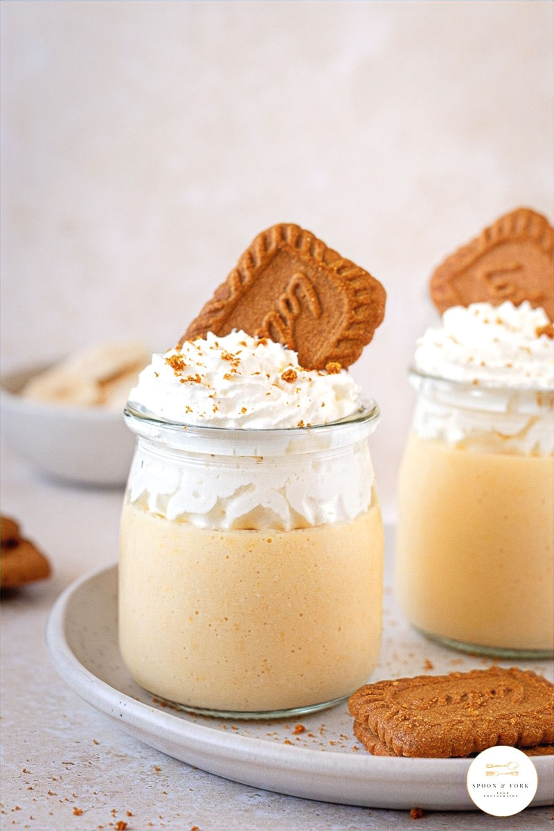 A banana mousse pot sat on plate with biscoff biscuits waiting to be served