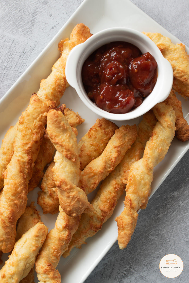 Some homemade cheese straws served on a white plate with tomato relish