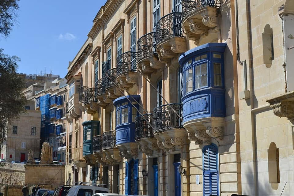 A row of terraced town houses in Valletta with blue venetian style balconies and sandstone walls.