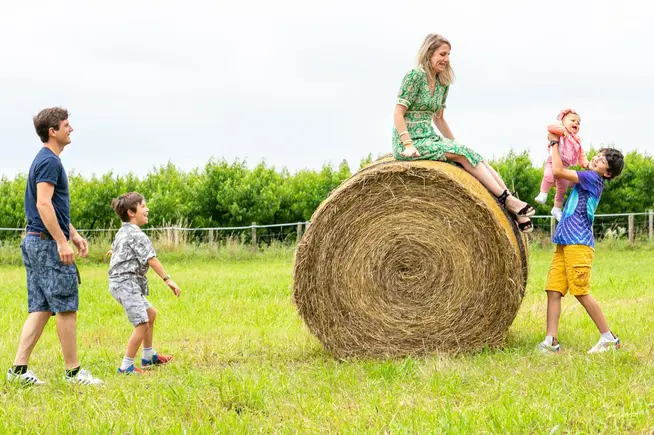 Famille jouant autour d’une botte de foin à la campagne