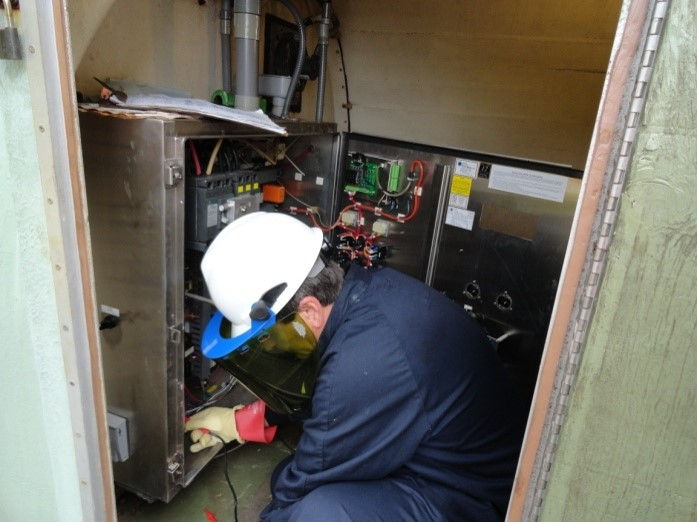 Man bent over in electrical cabinet performing a condition asessment.