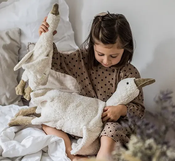 Girl cuddling two Senger Naturwelt white goose plush companions in bed