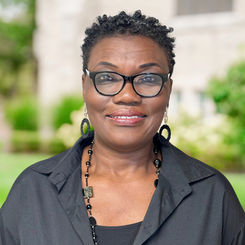 Smiling woman wearing glasses and black top in front of a building ABOUT Hardon Education