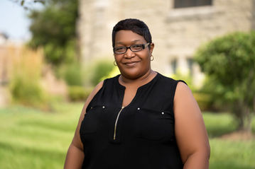 Smiling woman wearing glasses, black dress in front of a building. Hardon Education