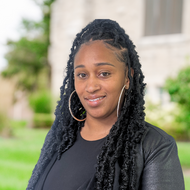 Smiling Black woman with long hair wearing a black top ABOUT Hardon Education