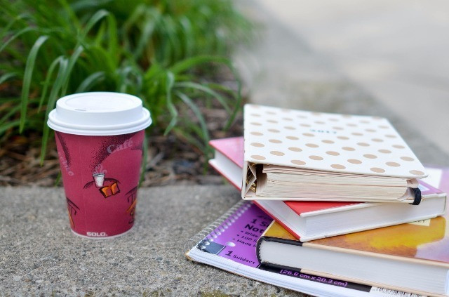 A to-go coffee mug and a stack of books outside.