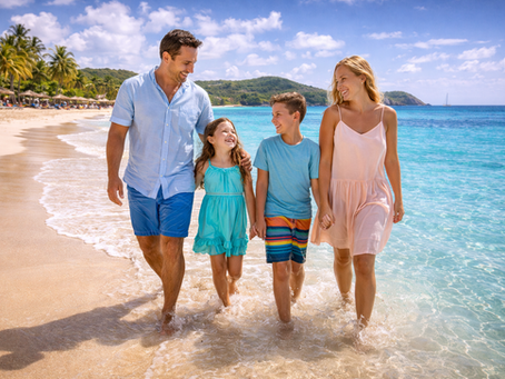A family smiling and walking together along the calm, shallow waters of a white-sand beach in Antigua.
