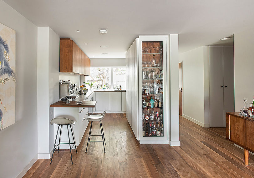 Galley run of bespoke kitchen by Jack Trench Design featuring integrated glass-fronted drinks cabinet with Corian-clad cabinetry and Silestone worktops