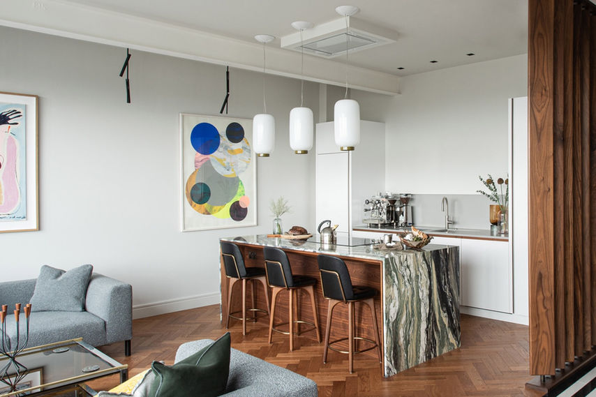 Side view of kitchen island featuring Jack Trench ‘Shell’ worktop design: cabinetry encased in a slender Luana Multicolour marble outer shell with no visible joins; open-plan living area in foreground.