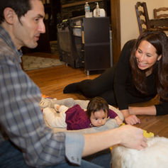 Smiling woman and man playing with a baby on a wooden floor.