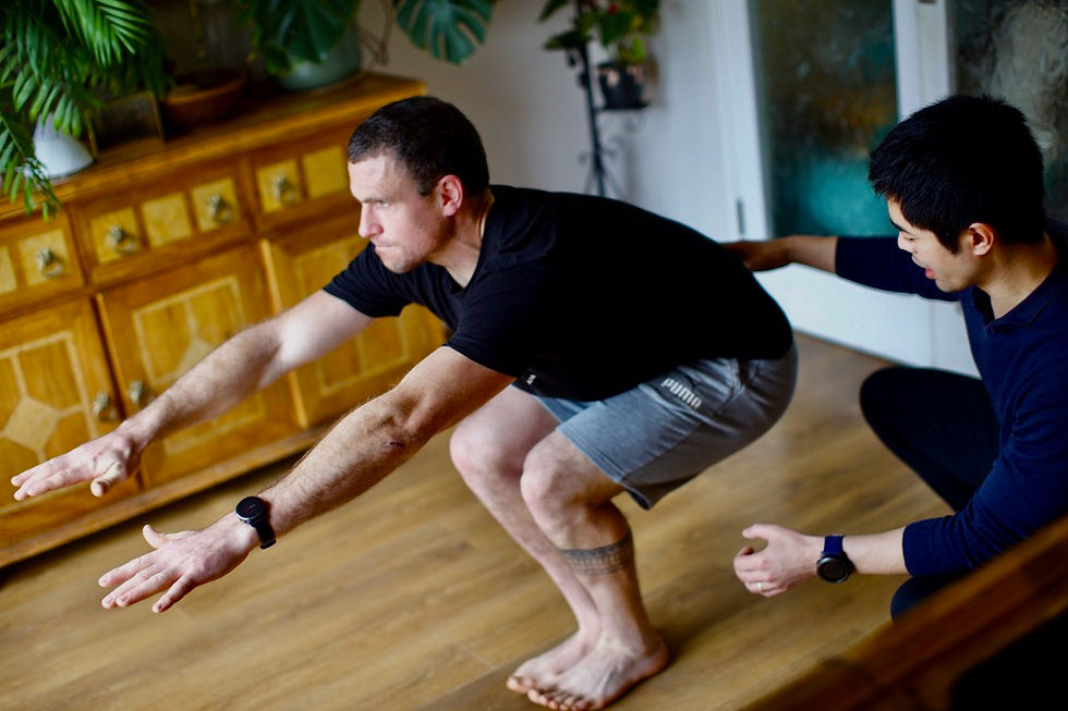 A physiotherapist supports a young, male patient's back as they perform a squat.
