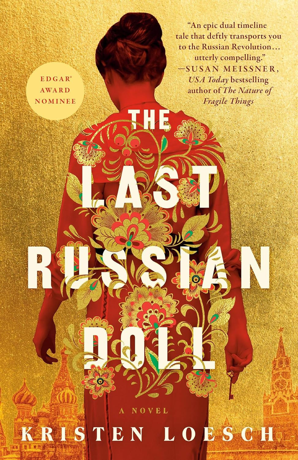 A young woman with her hair in a bun, dressed in a red robe overlaid with embroidery patterns, against a golden background where the outlines of the Moscow Kremlin are barely visible; she holds a key in one hand; cover of The Last Russian Doll