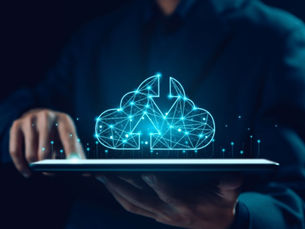 A person in a dark suit holds a tablet with a glowing blue cloud and circuit pattern above it, suggesting digital technology or data.