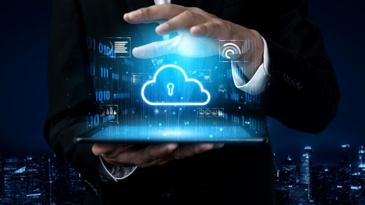 A person in a suit uses a tablet displaying a glowing cloud icon with a lock, symbolizing data security. Cityscape background at night.