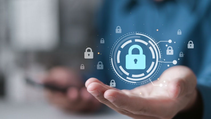 A hand holds a holographic lock icon, symbolizing digital security. The background is blurred, featuring blue tones, giving a tech-focused mood.