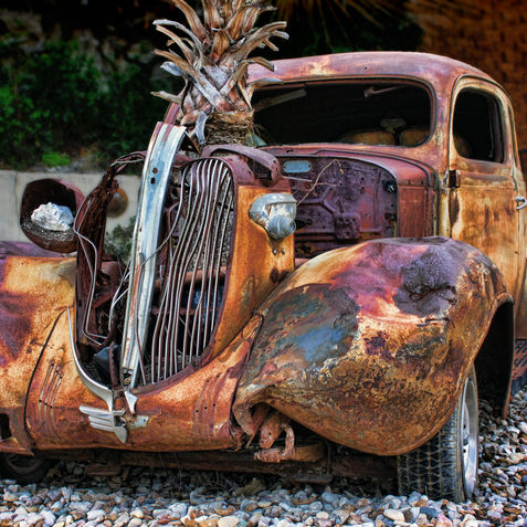 A very old broken down rusty car displayed as a sculpture.