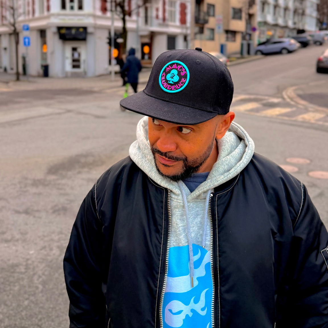 A man wearing the Mac's Club Deuce logo in Miami Vice pink and blue on a snapback baseball cap.