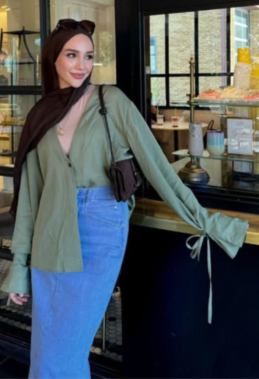 Woman wearing a modest outfit with an olive green button-up shirt, white denim midi skirt, brown hijab, and crossbody bag, styled for a casual everyday look.