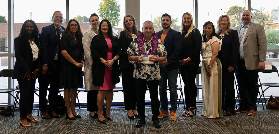 Tom Phillips, Bellflower Unified School District’s Teacher of the Year, stands with district leaders at the STAR Awards ceremony, holding his award and wearing a purple lei.