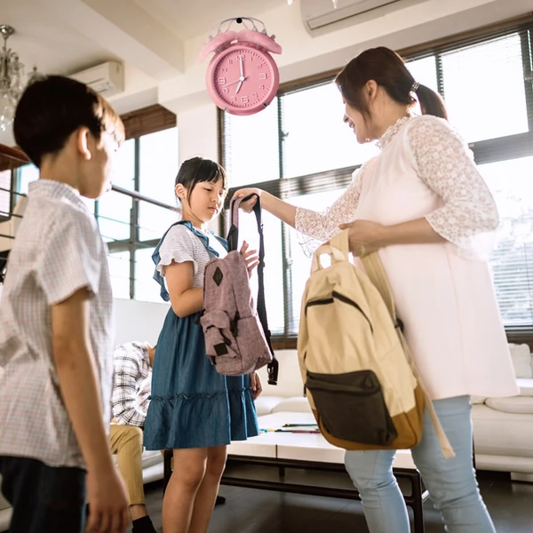 A mother is helping her children get ready for school in a bright, organized living room. She hands 