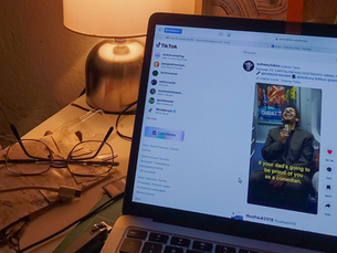 TikTok open on laptop in a low-lit room with a warm lamp and reading glasses