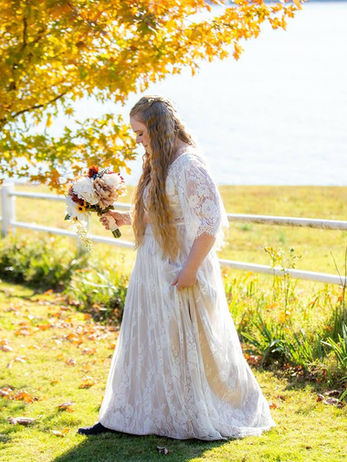 Bride in white dress holding flowers near a lake in fall Our Real Brides