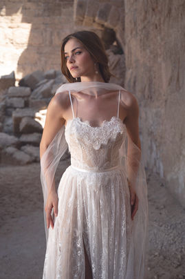 Bride wearing a romantic Lace & Love by Shany Sasson gown with a sheer tulle shawl, posing against ancient stone ruins.