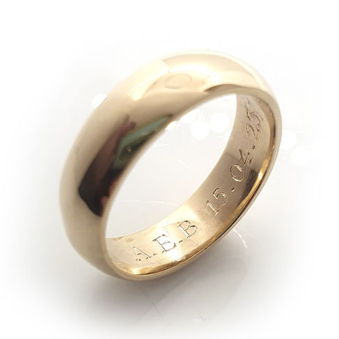A gold wedding ring engraved with a wedding date and initials