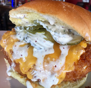 Delicious fried chicken sandwich with cheese and sauce on a white plate.