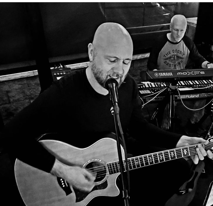 Bald man singing and playing acoustic guitar with keyboardist