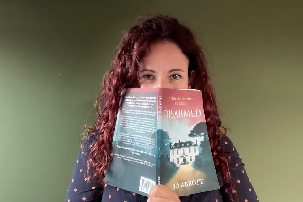 Woman with curly hair holding a book titled "Disarmed" by Jo Abbott, partially covering her face. Green background, calm expression.