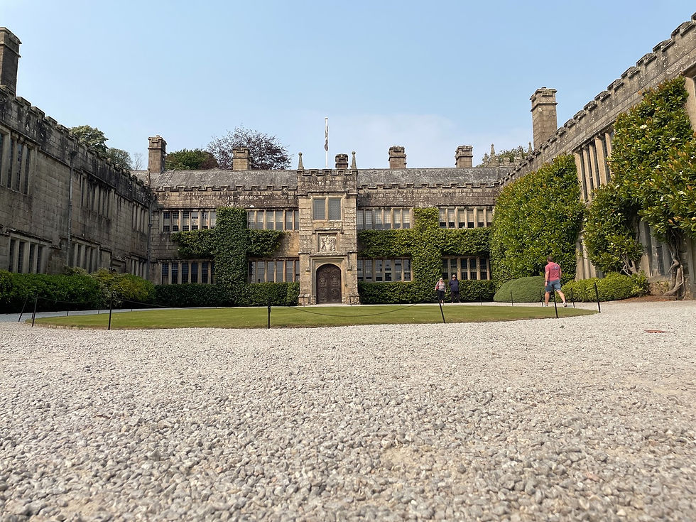 Stone courtyard of a historic building with ivy-covered walls. Two people walk on the green lawn under a clear blue sky. Peaceful setting.