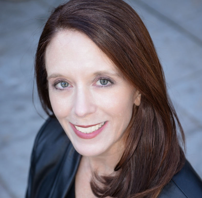 Smiling woman with long brown hair and a black jacket. Close-up with a blurred gray background, conveying a friendly and warm mood.
