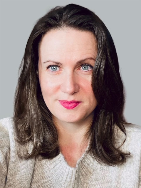 White woman with small smile, dark shoulder length hair and blue-green eyes