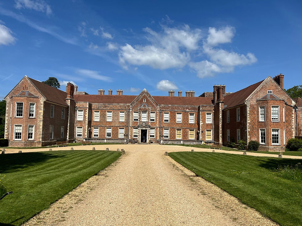 Historic brick mansion under blue sky, with symmetrical windows and a gravel path leading to the entrance, surrounded by manicured lawns.