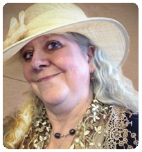 Smiling woman in a beige hat with a floral pattern, wearing a lace-trimmed outfit. Neutral background. Elegant and joyful expression.