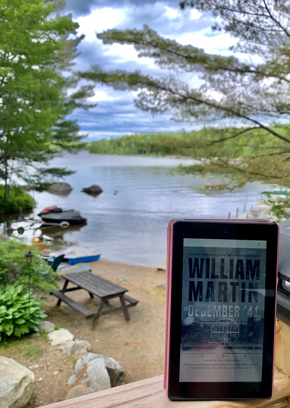 Kindle with December '41 cover on rail in front of lake in Maine.