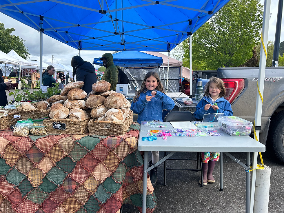 Arielle and Élyssa grinning proudly behind their table — bead animals and bracelets ready for their first market day.
