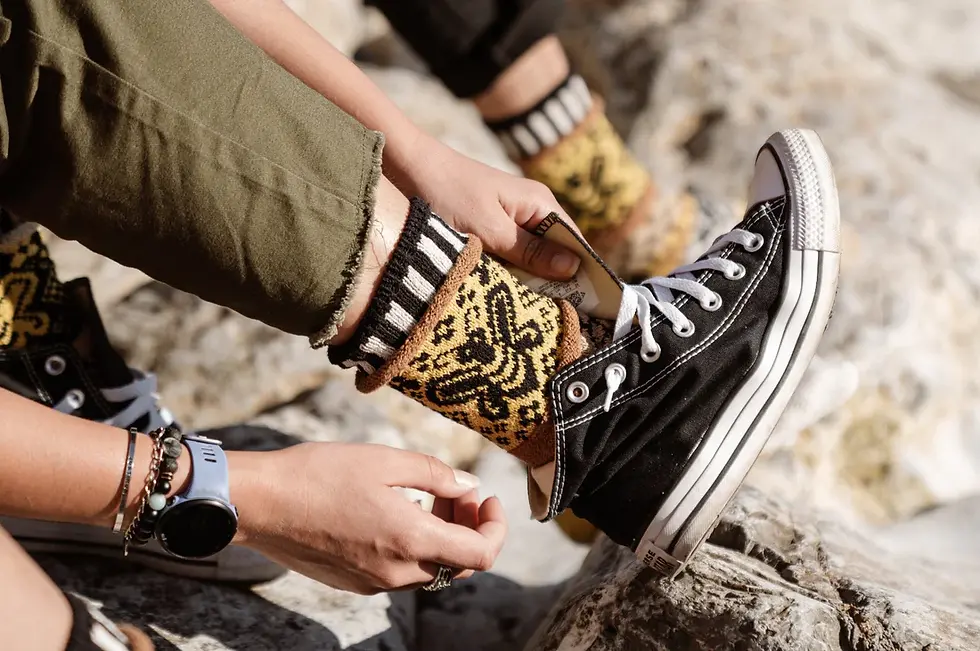 Model's feet wearing mismatched crew socks in yellow & black with knit pattern of bees & honeycomb