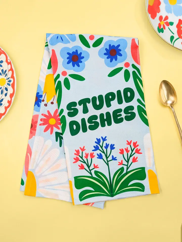 Folded Stupid Dishes tea towel styled on a kitchen table at Tickled Pink Ottawa.