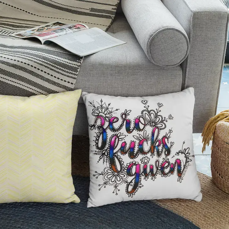 Pillow stamped with black & white Zero Fucks Given design on floor beside couch