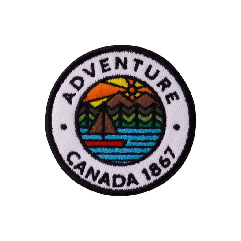 Round black & white embroidered patch with sailboat scene on lake with mountains & sun, text, 'Adventure' & 'Canada 1867'