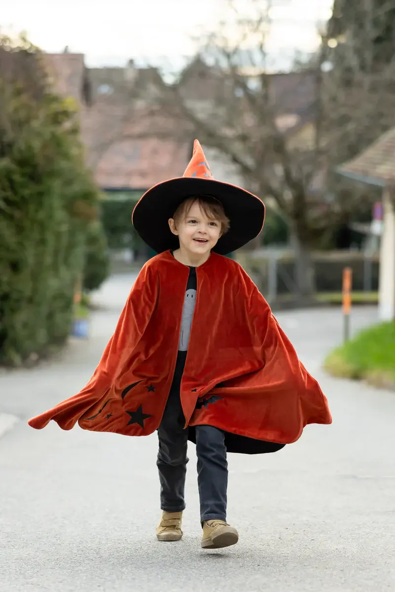 Little boy wearing orange & black wizard cloak & pointed hat set