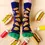 Thumbnail: Top view of feet wearing navy socks with print of all-dressed hamburgers surrounded by hotdogs, mustard & ketchup bottles