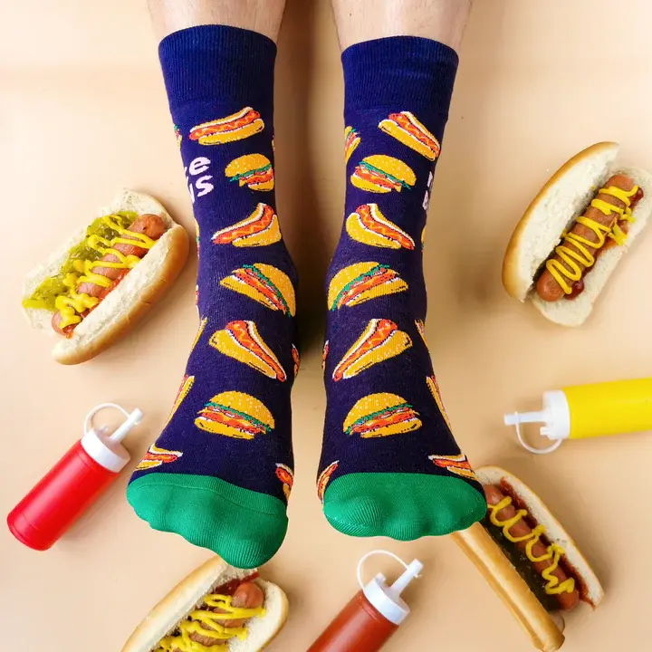Top view of feet wearing navy socks with print of all-dressed hamburgers surrounded by hotdogs, mustard & ketchup bottles